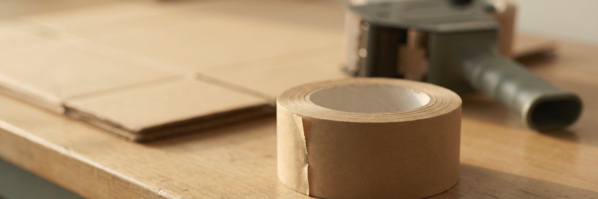 The corner of a packing bench with a roll of packing tape and a tape gun.
