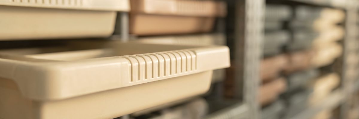 The front lip of a plastic parts tray pulled slightly out from a shelf of identical trays.