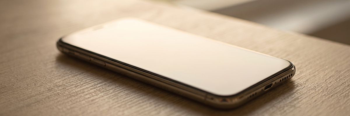 A phone lying face up on a desk, its screen a blank pale glow.