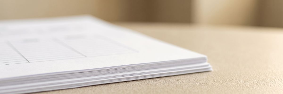 The corner of a stack of freshly printed sheets on a desk, faint table rules just visible.
